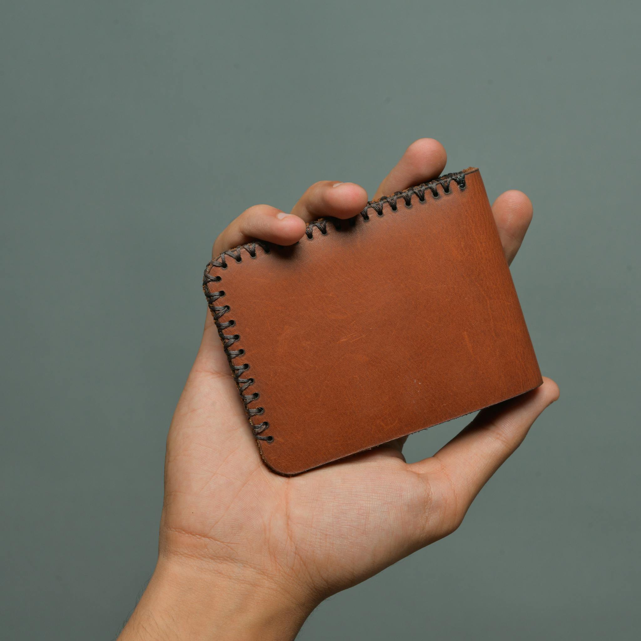 Close-up of a hand holding a handmade leather wallet against a gray background.